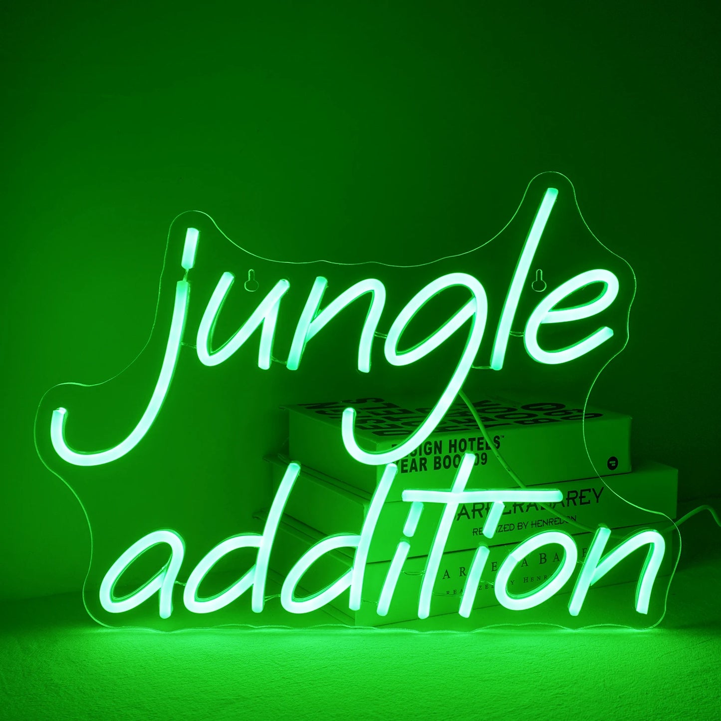 Ein leuchtend grünes LED-Neonschild „Jungle Addition“ vor einem minimalistischen weißen Wandhintergrund.