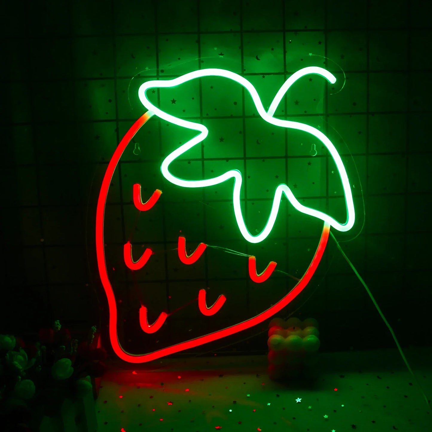 Ein leuchtendes LED-Neonschild in Form einer Erdbeere mit einem leuchtend roten Körper und üppigen grünen Blättern darauf.