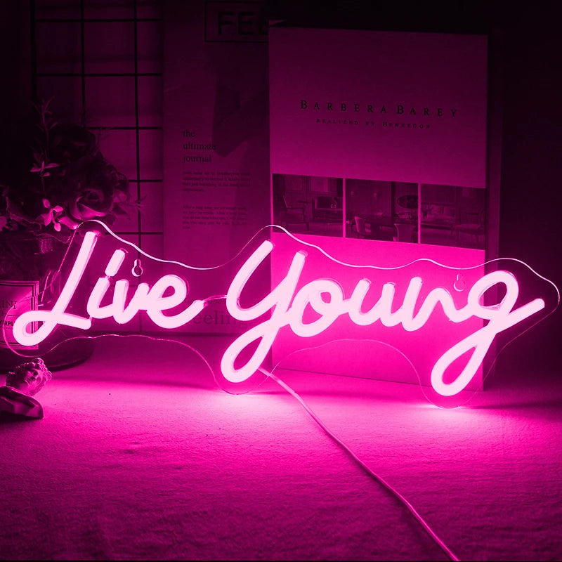 Das Bild zeigt ein leuchtendes, handgefertigtes LED-Neonschild mit dem Satz „Live Young“ in einer lebendigen, kursiven Schrift.