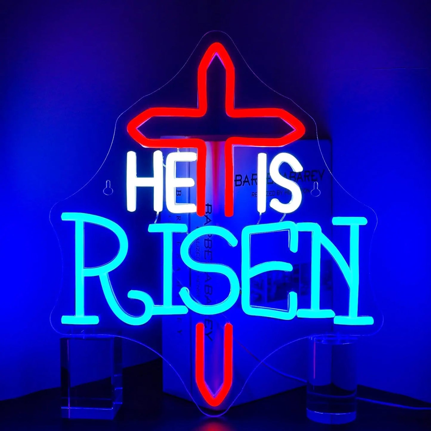 Das Bild zeigt ein leuchtendes LED-Neonschild mit der Aufschrift „He Is Risen“, das in kräftigen, warmen Farbtönen leuchtet.