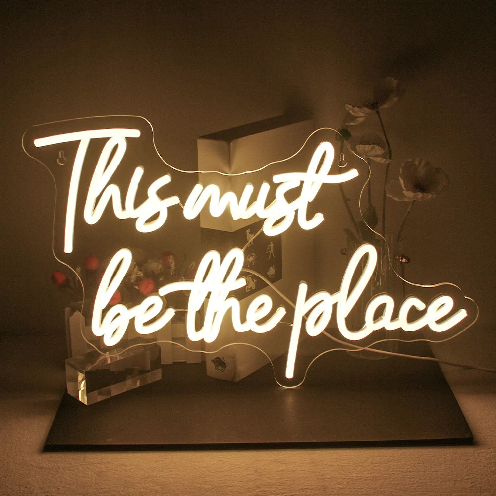 Das Bild zeigt ein leuchtendes LED-Neonschild mit der Aufschrift „Dies muss der Ort sein“ in Schreibschrift.