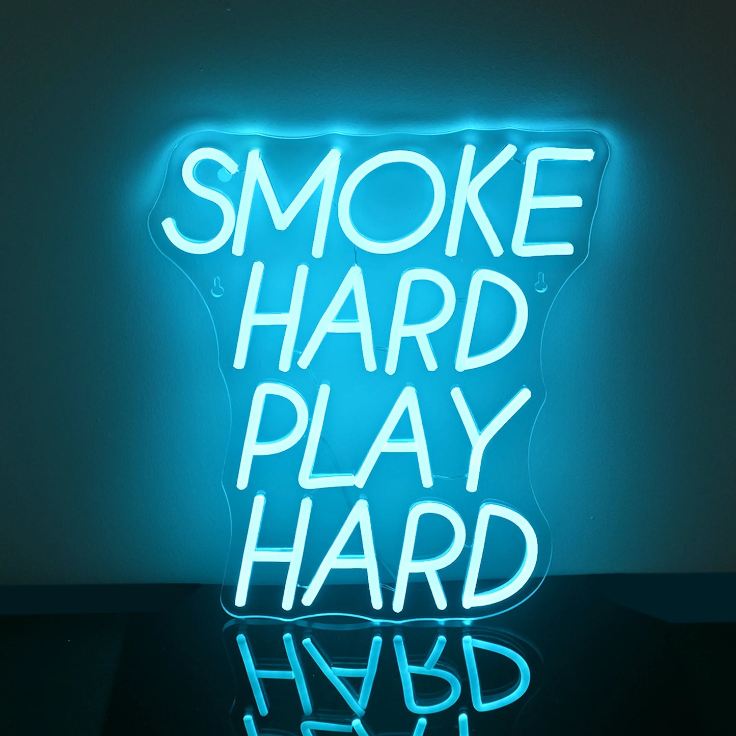 Das Bild zeigt ein leuchtendes LED-Neonschild mit der Aufschrift „Smoke Hard Play Hard“ in fetten Großbuchstaben.