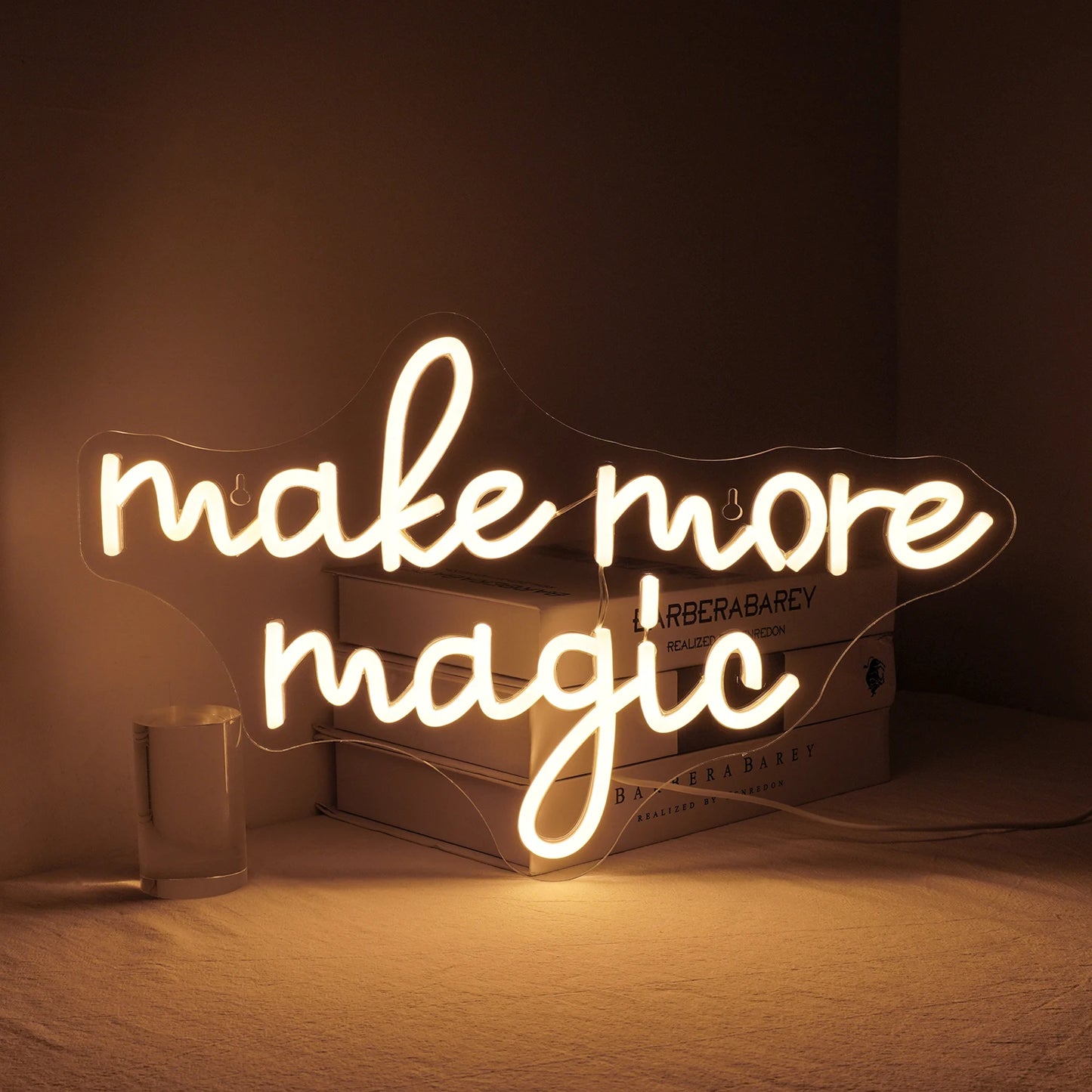 Ein leuchtendes LED-Neonschild mit der Aufschrift „Make More Magic“ in einem lebhaften Farbmix ist vor einem glatten, dunklen Hintergrund angebracht.
