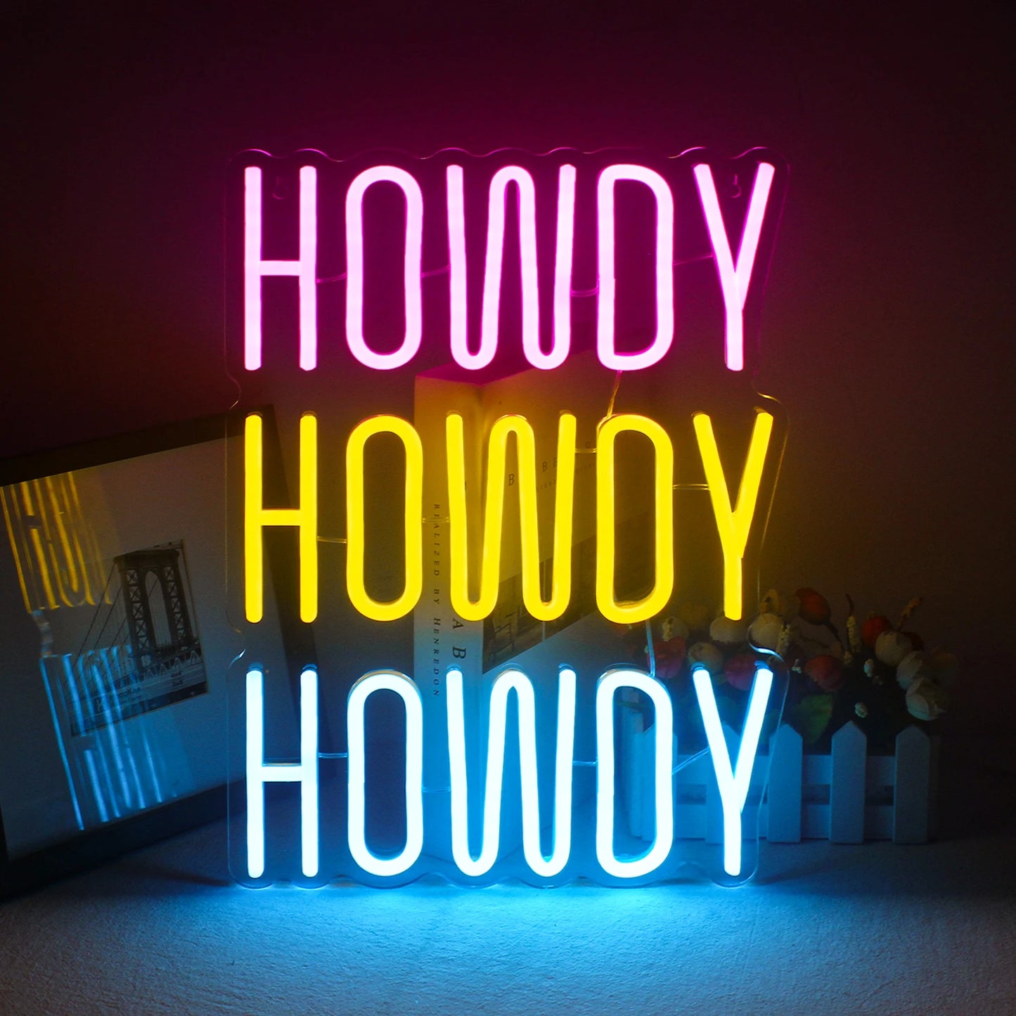 Ein lebendiges, handgefertigtes LED-Neonschild mit dem Wort „Howdy“ in einer verspielten, kursiven Schriftart.