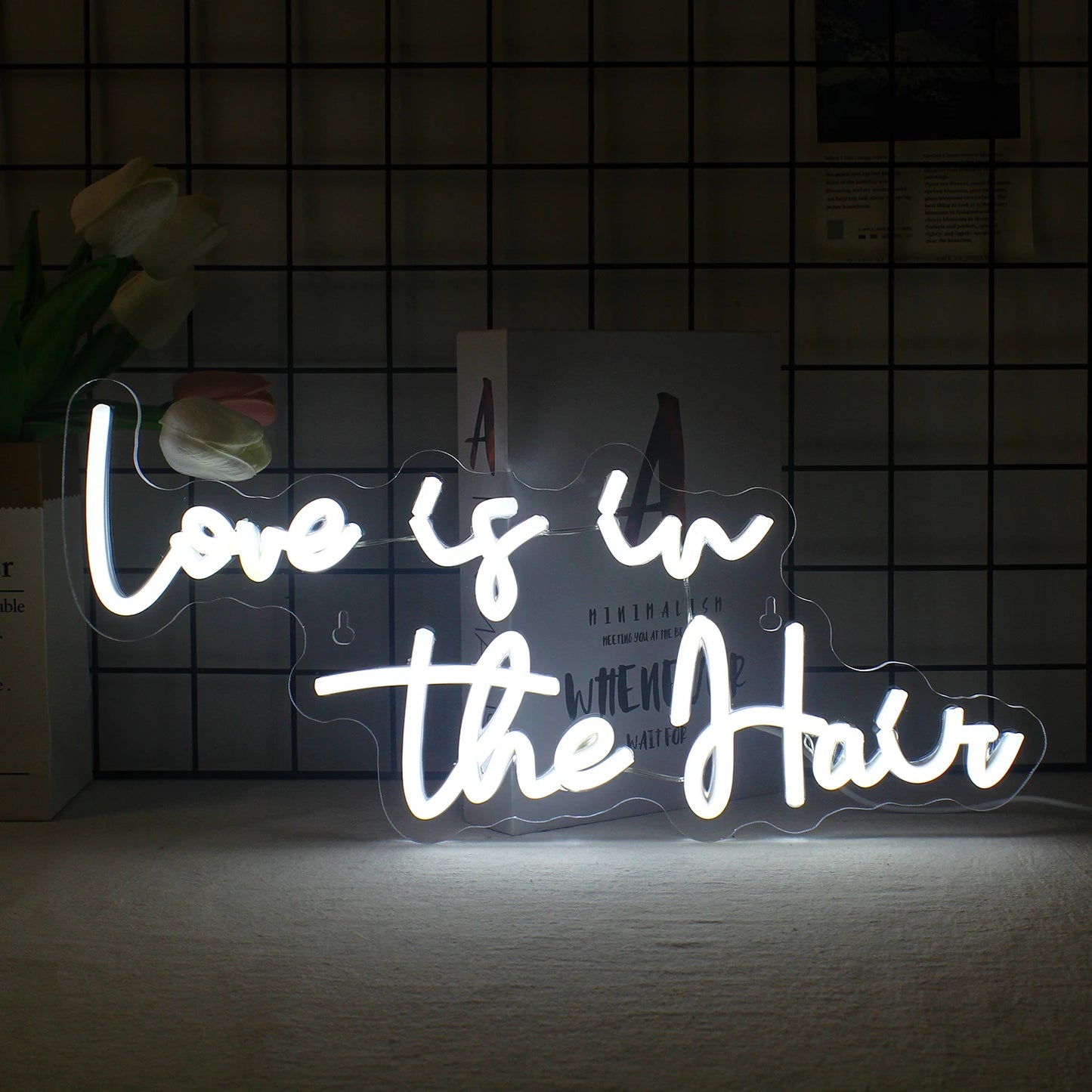 Das Bild zeigt ein leuchtendes LED-Neonschild, auf dem in stilvoller, fließender Schrift der Satz „Love is in the Hair“ steht.