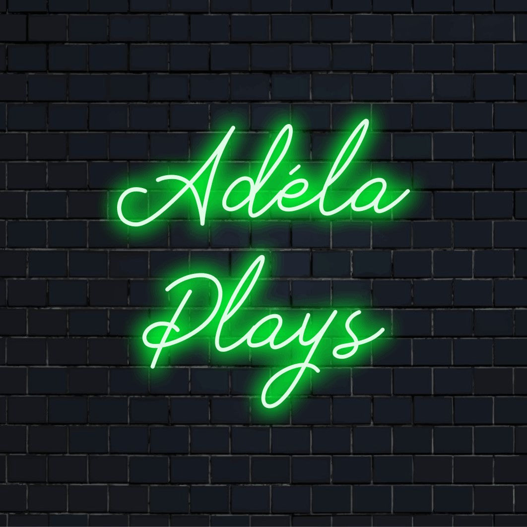 Adela Plays Custom Name Neon Sign, bright neon glow on dark brick wall