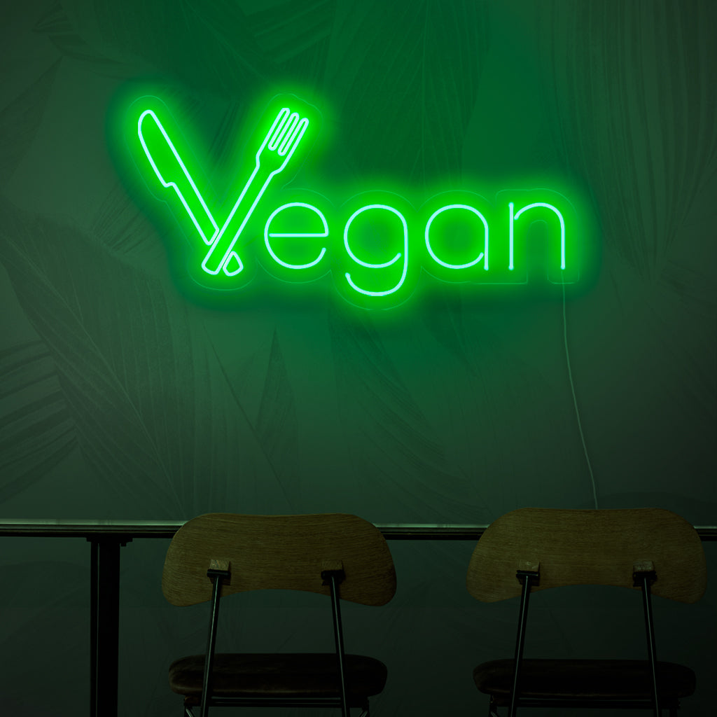 Ein Neonschild mit der Aufschrift „Vegan“, das mit seinem leuchtend grünen Licht das Konzept der pflanzlichen Küche repräsentiert.
