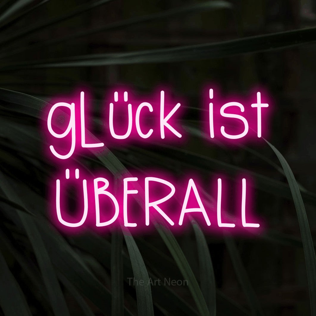 LED neon sign reading “glück ist ÜBERALL”, arranged in 2 lines.