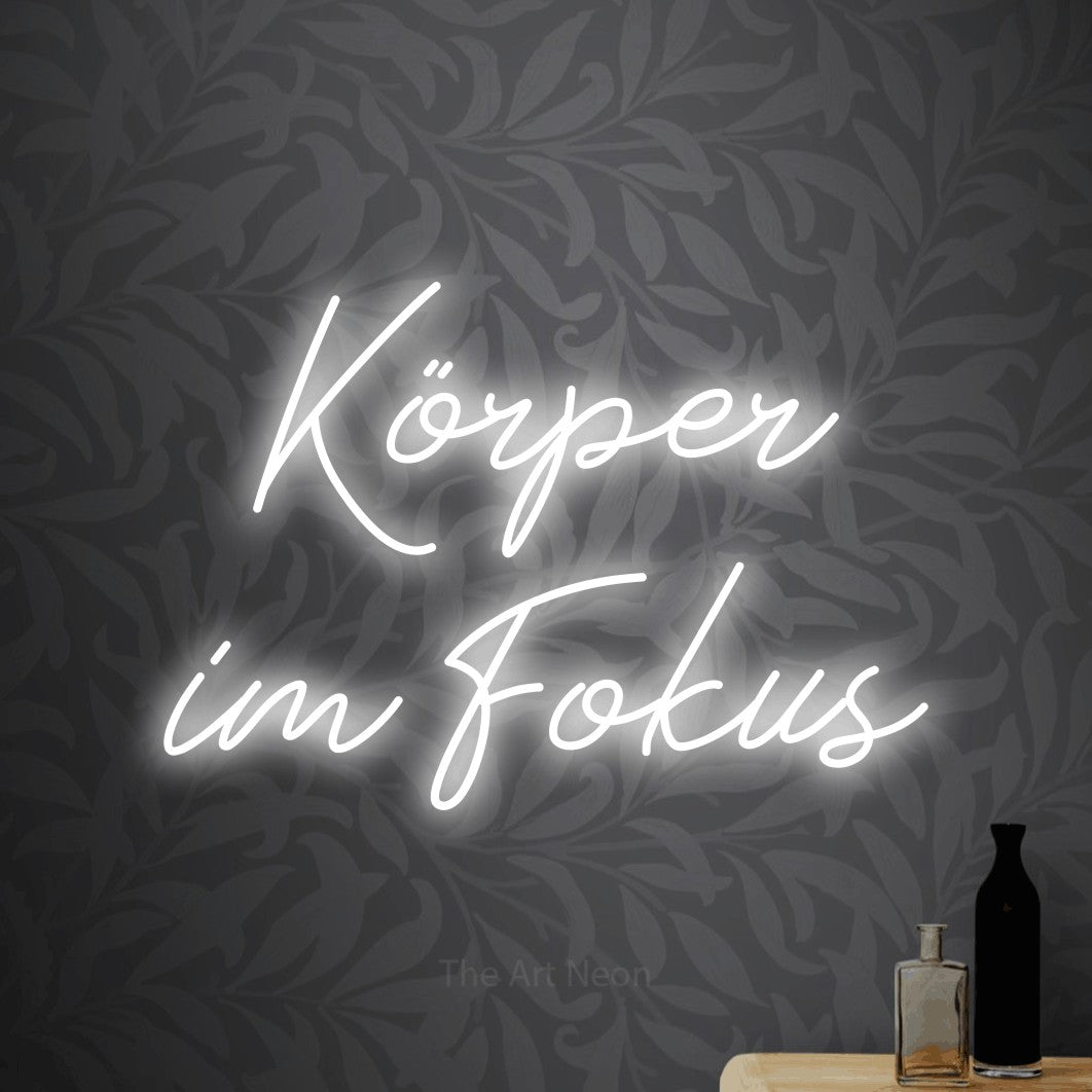 LED neon sign reading “Körper im Fokus”, arranged in 2 lines.