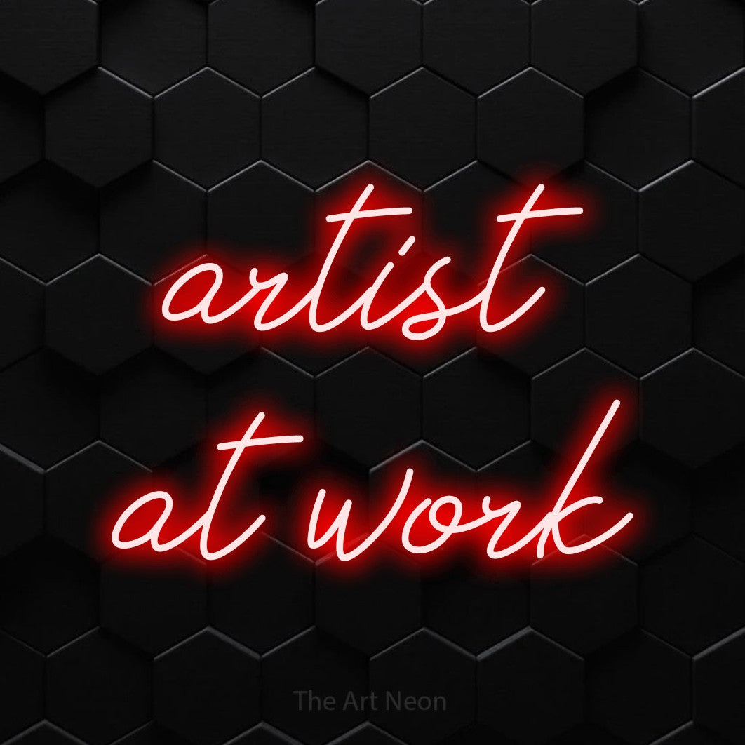LED neon sign reading “artist at work”, arranged in 2 lines.