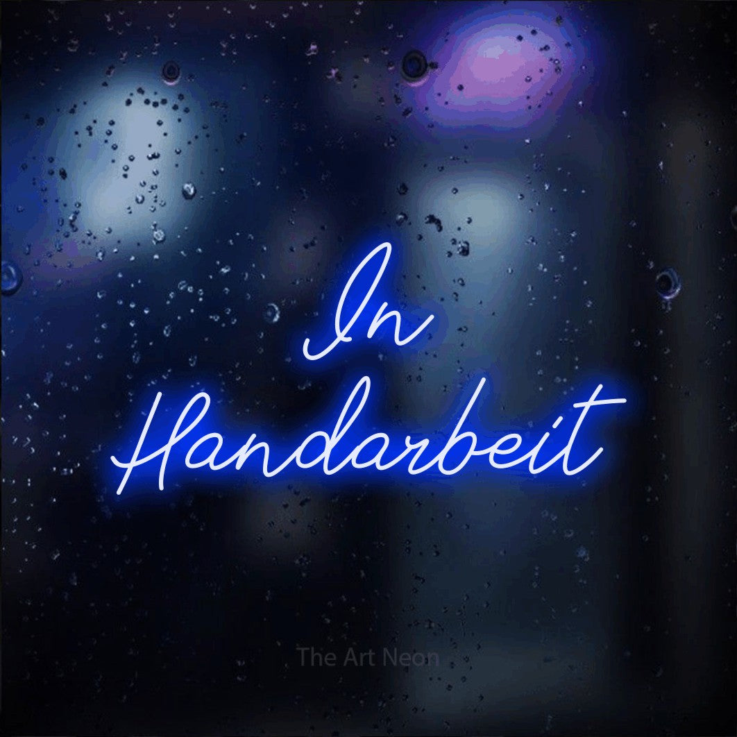 LED neon sign reading “In Handarbeit”, arranged in 2 lines.