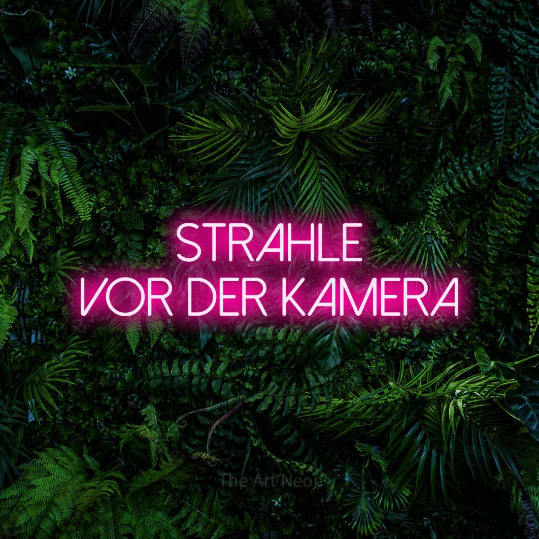LED neon sign reading “Strahle vor der Kamera”, arranged in 2 lines.