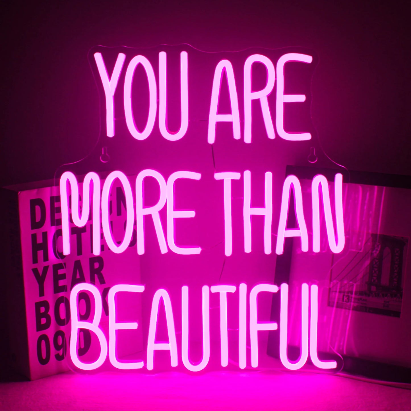 The image features a vibrant LED neon sign displaying the phrase "You Are More Than Beautiful.