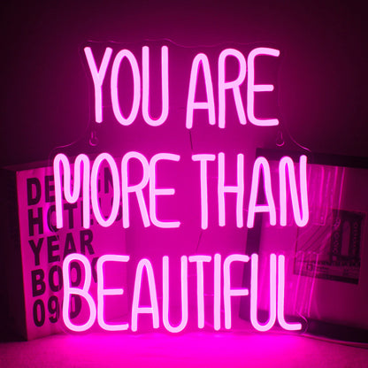 The image features a vibrant LED neon sign displaying the phrase "You Are More Than Beautiful.