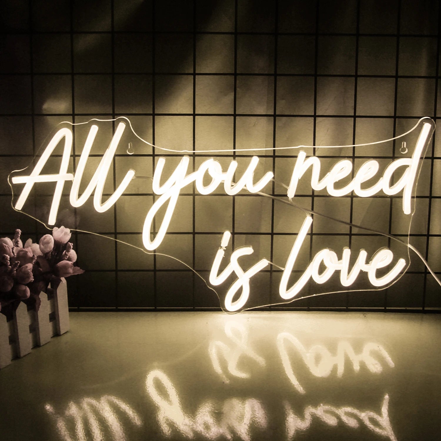 The image features a vibrant LED neon sign displaying the text "You Need Is Love" in bright, glowing letters.