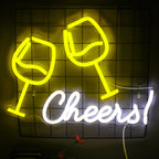 An einer Backsteinwand ist ein leuchtendes LED-Neonschild mit der Aufschrift „Cheers“ in einer verspielten Schreibschrift angebracht.