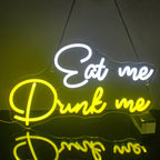Das Bild zeigt ein leuchtendes LED-Neonschild mit den Worten „Eat Me Drink Me“ in einer skurrilen Schreibschrift.