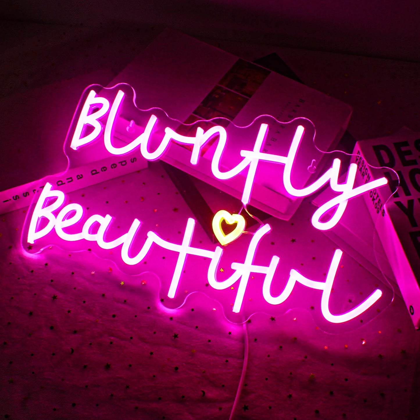 The image features a vibrant, handmade LED neon sign displaying the phrase "Bluntly Beautiful.