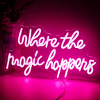 The image features a vibrant LED neon sign that reads "Where The Magic Happens" in an elegant, playful script font.