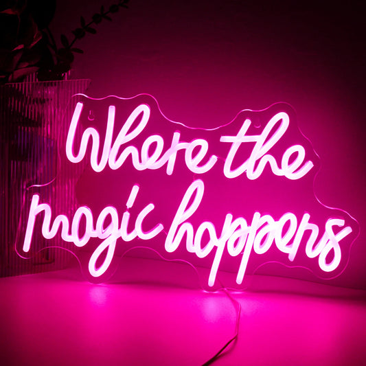 The image features a vibrant LED neon sign that reads "Where The Magic Happens" in an elegant, playful script font.