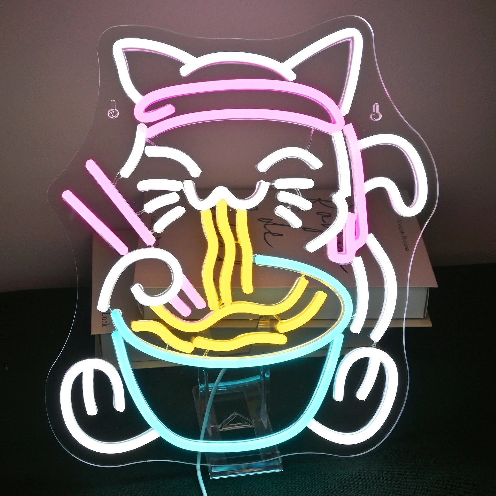 Das Bild zeigt ein lebendiges und farbenfrohes LED-Neonschild mit dem skurrilen Design einer Katze, die eine Schüssel Ramen genießt.