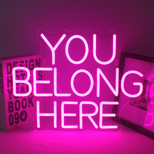 A vibrant LED neon sign displaying the words "You Belong Here" in a warm, inviting script font.