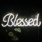 An einer dunklen Wand ist ein leuchtendes LED-Neonschild mit der Aufschrift „Blessed“ angebracht, das ein warmes, einladendes Licht ausstrahlt.