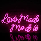 The image features a vibrant LED neon sign displaying the words "Love Made Me Do It" in a stylish cursive font.