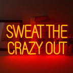 A vibrant LED neon sign displaying the phrase "Sweat The Crazy Out" in a playful cursive font.
