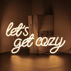 Das Bild zeigt ein leuchtendes LED-Neonschild mit dem Satz „Let’s Get Cozy“ in einer warmen, einladenden Schreibschrift.