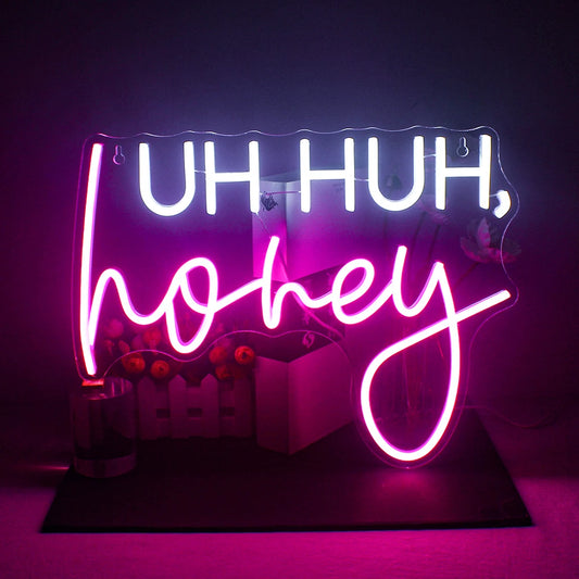 The image features a vibrant, handmade LED neon sign displaying the phrase "Uh Huh" in a lively cursive script.