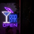 Das Foto zeigt ein Neonschild mit einem Cocktail mit Schirmchen auf der linken Seite und dem Text „Open Bar“ auf der rechten Seite. Dieses Neonschild ist ideal für Bars im Innen- und Außenbereich.