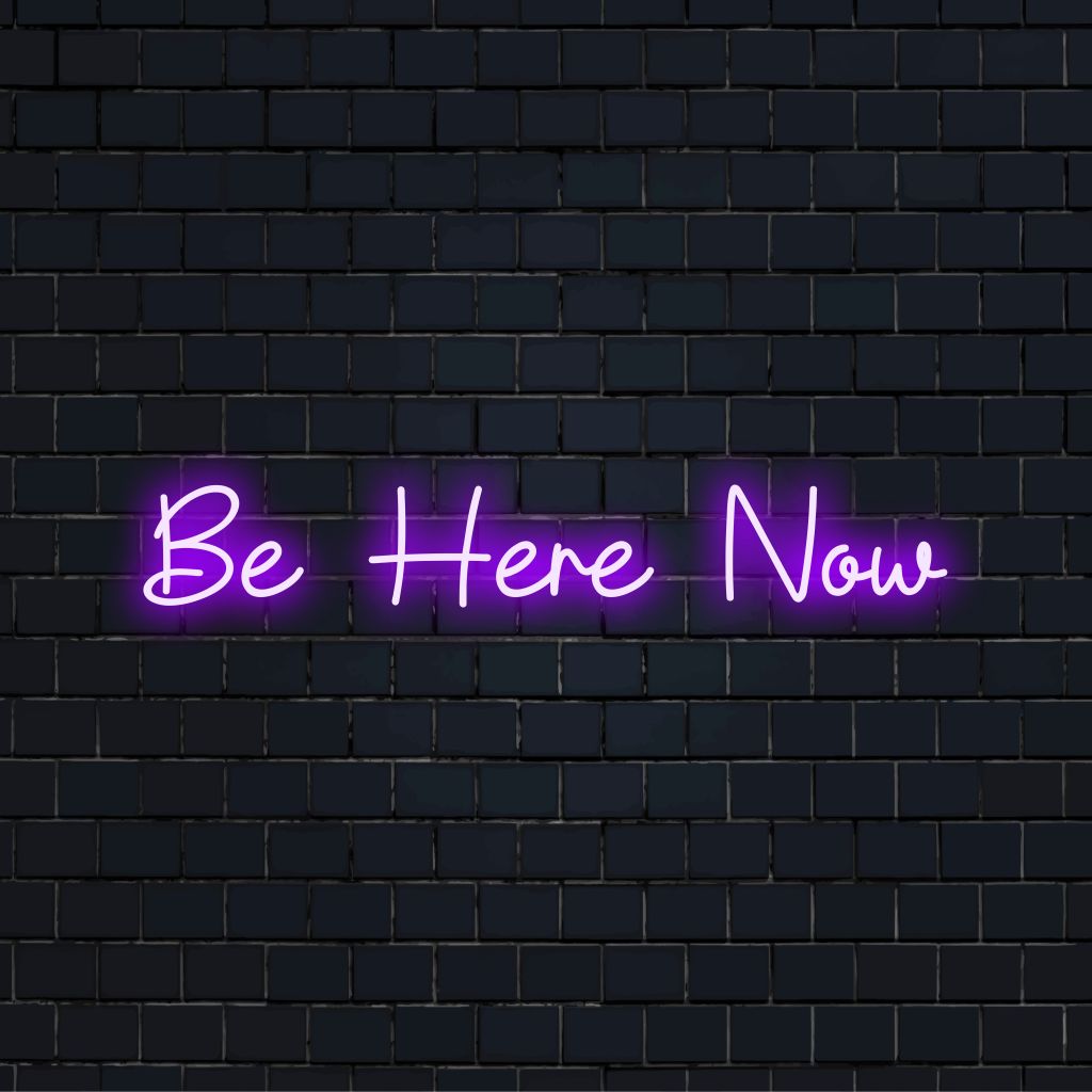 Be Here Now LED Neon Sign, glowing lettering on dark brick wall