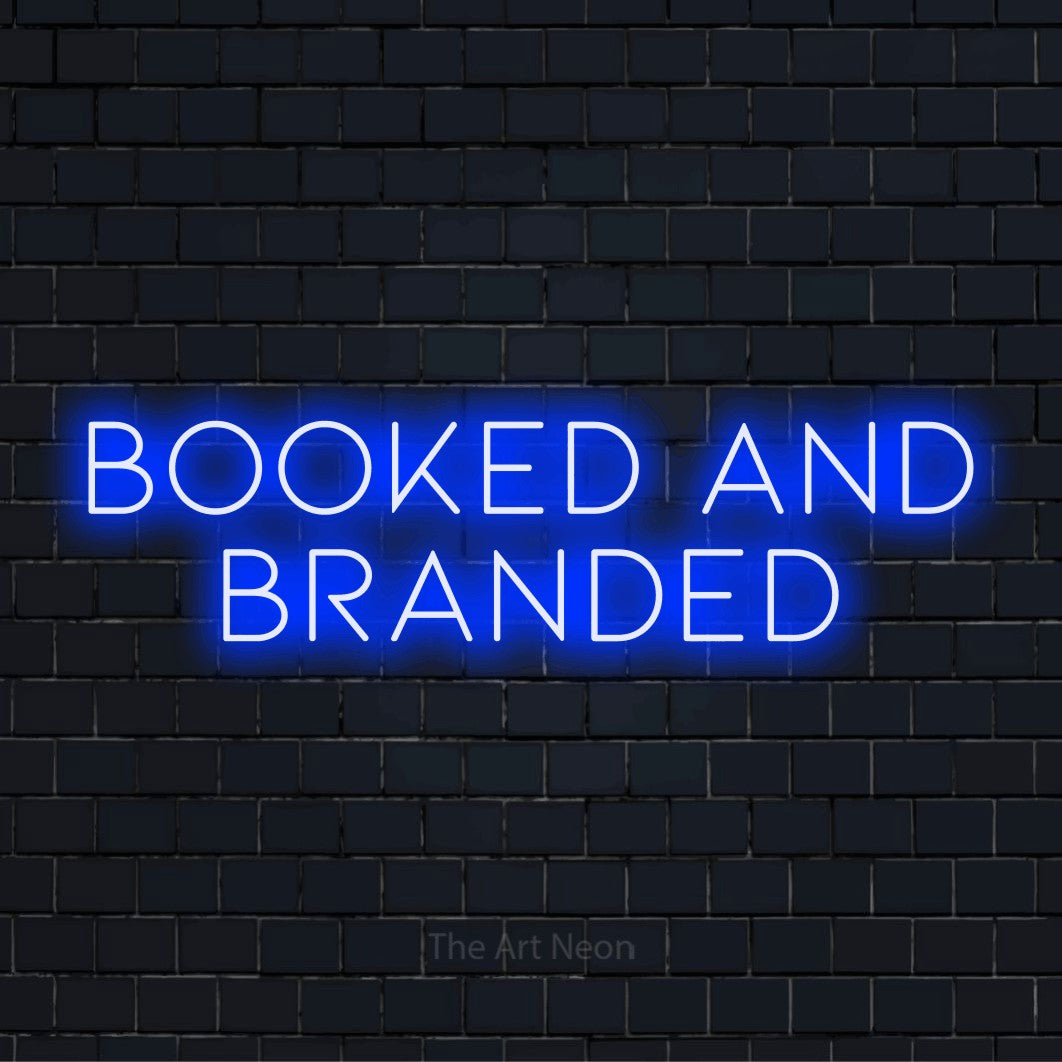 "Booked And Branded" LED neon sign on a black brick wall
