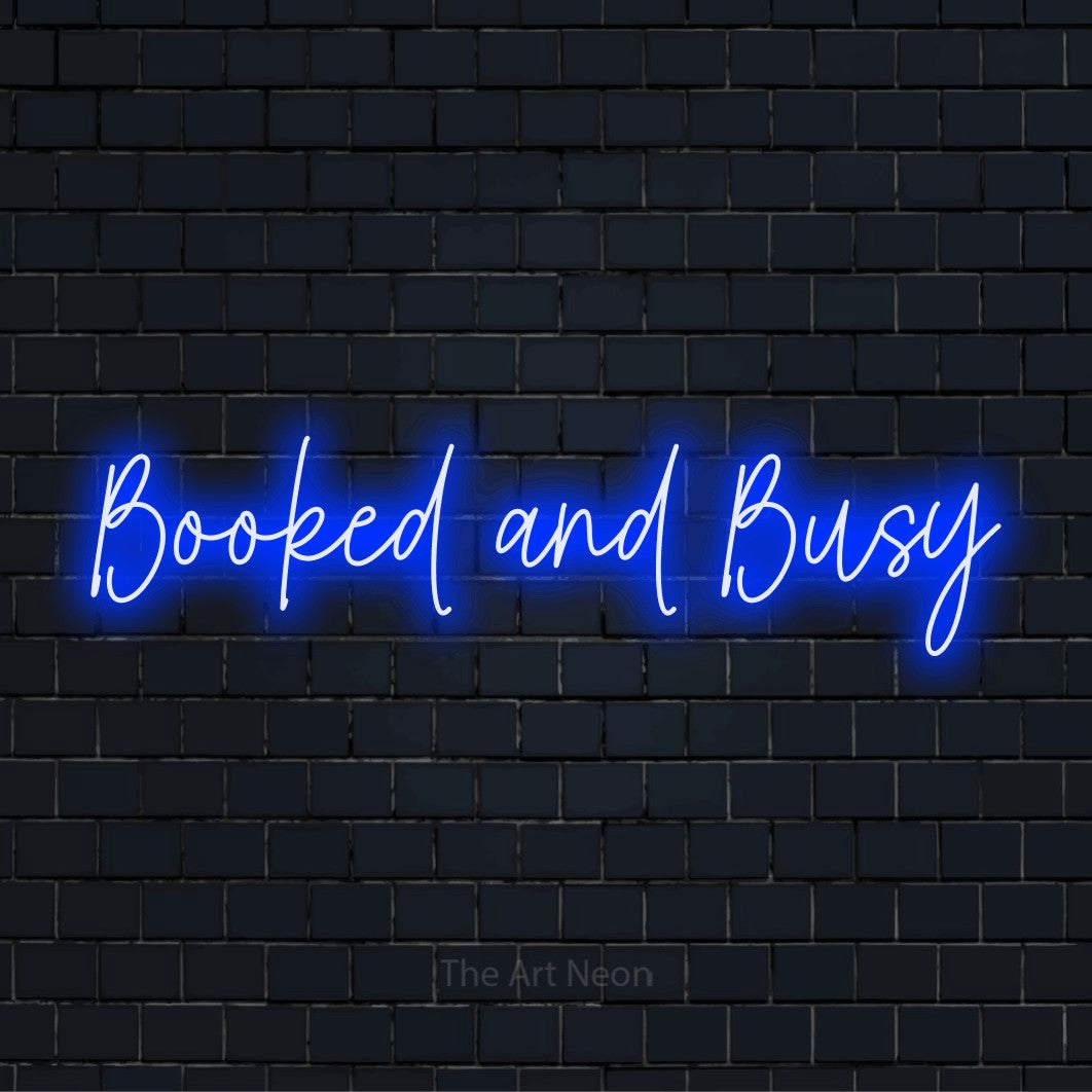 "Booked And Busy" glowing LED neon sign on a black brick wall