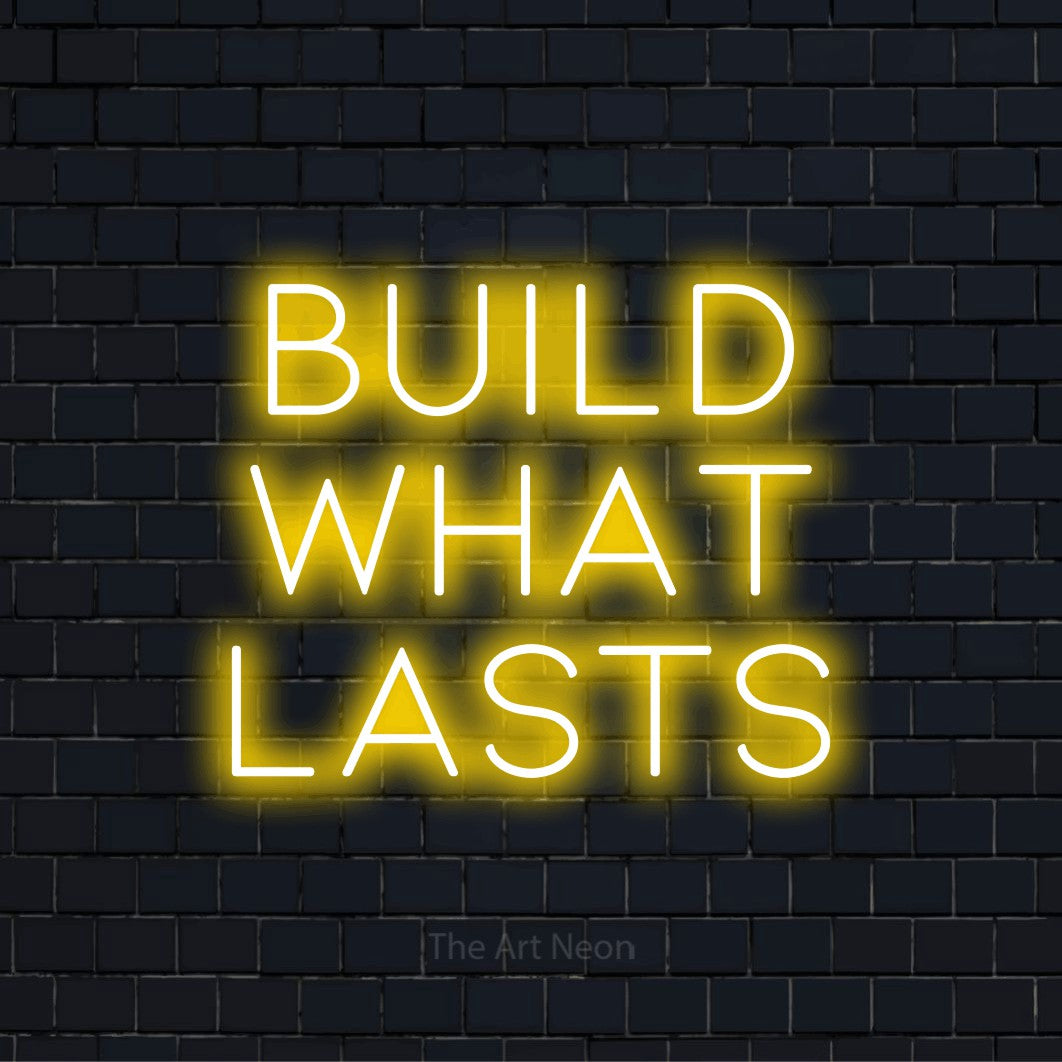 "Build What Lasts" text design with neon effect on a black brick wall