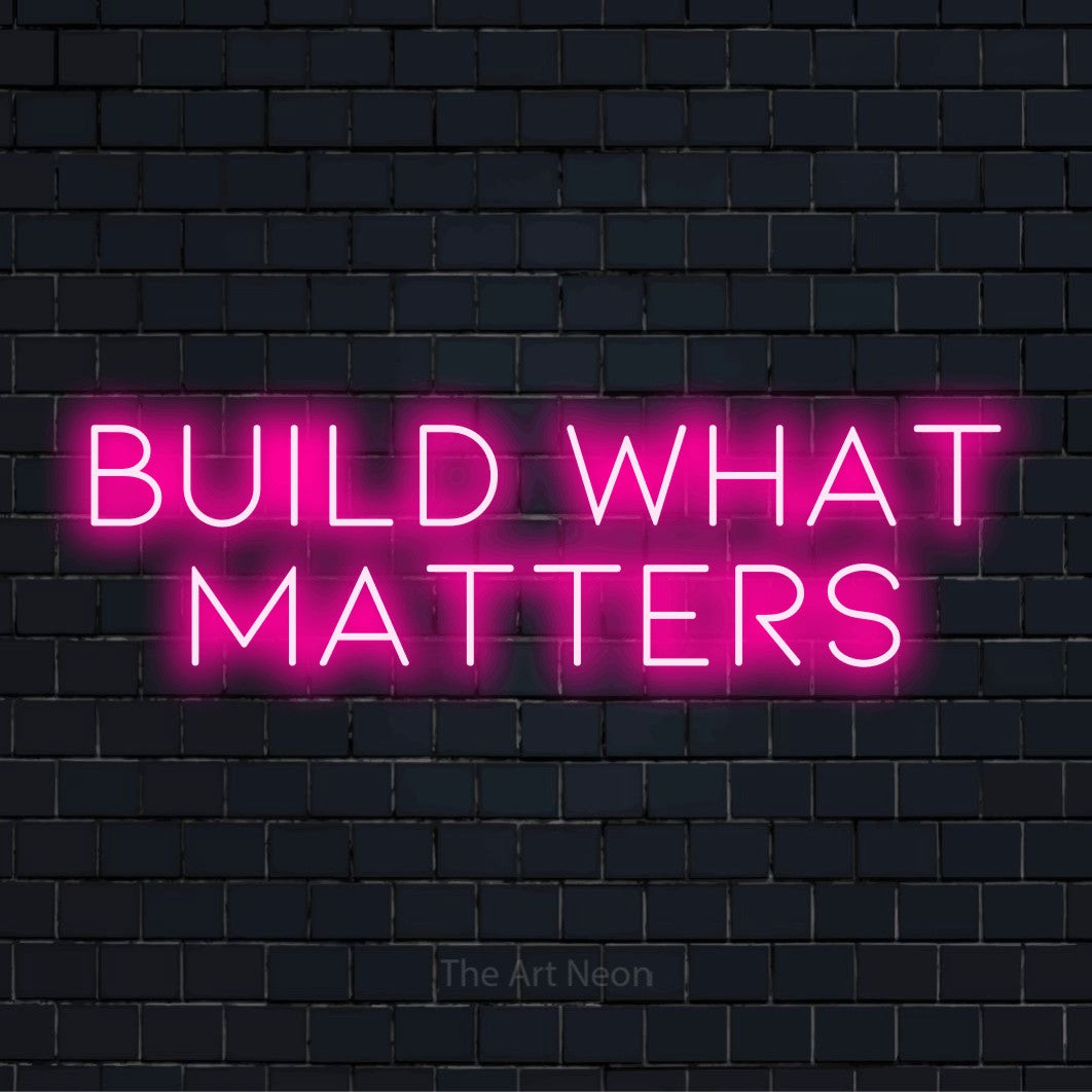 "Build What Matters" neon text design on a black brick wall
