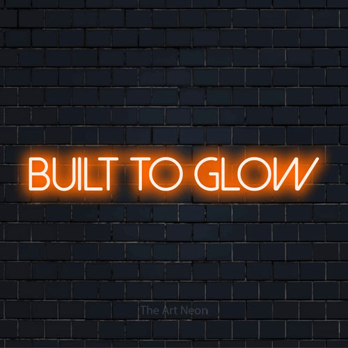 "Built To Glow" text design with neon effect on a black brick wall