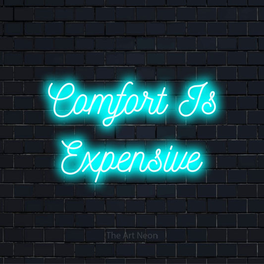 "Comfort Is Expensive" text design with neon effect on a black brick wall