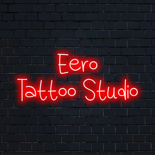 Eero Tattoo Studio Personalized LED Neon Sign, glowing neon text against black brick wall
