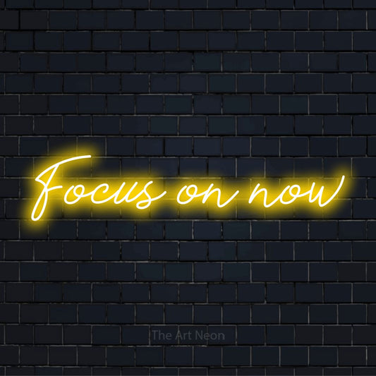 "Focus On Now" neon text design on a black brick wall