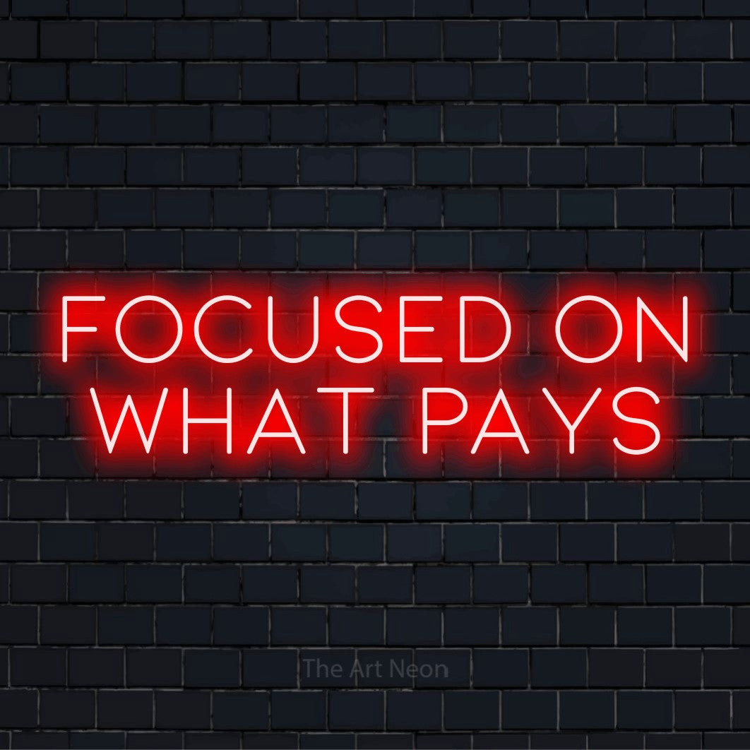 "Focused On What Pays" LED neon sign on a black brick wall