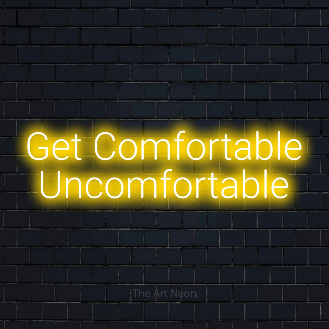 "Get Comfortable Uncomfortable" script-style LED neon sign on a black brick wall