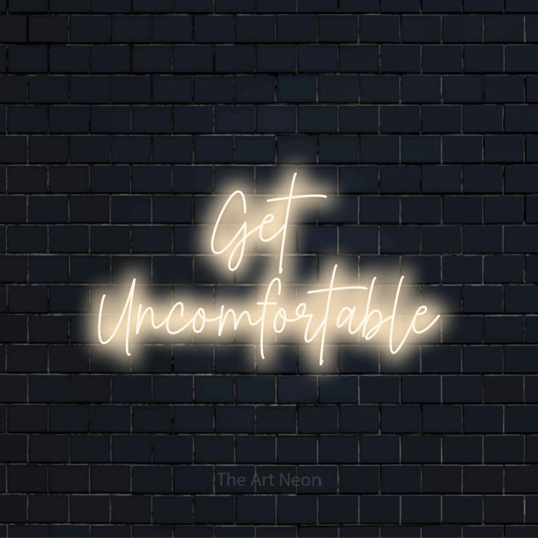 "Get Uncomfortable" neon text design on a black brick wall