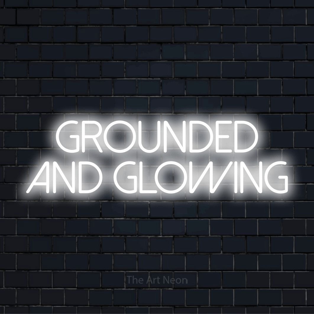 "Grounded And Glowing" script-style LED neon sign on a black brick wall
