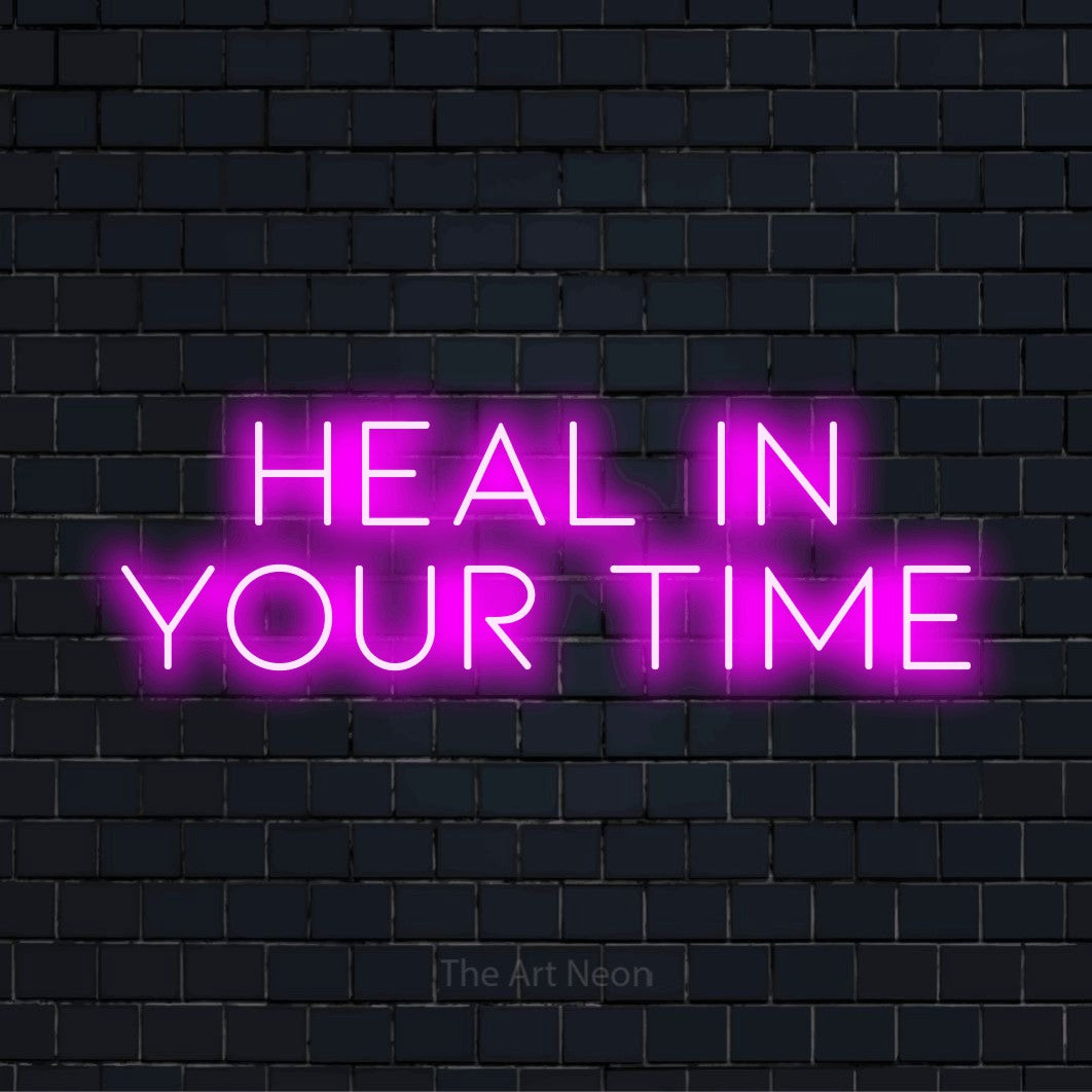 "Heal In Your Time" script-style LED neon sign on a black brick wall