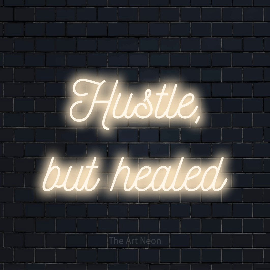 "Hustle, But Healed" script-style LED neon sign on a black brick wall