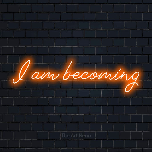 "I Am Becoming" script-style LED neon sign on a black brick wall