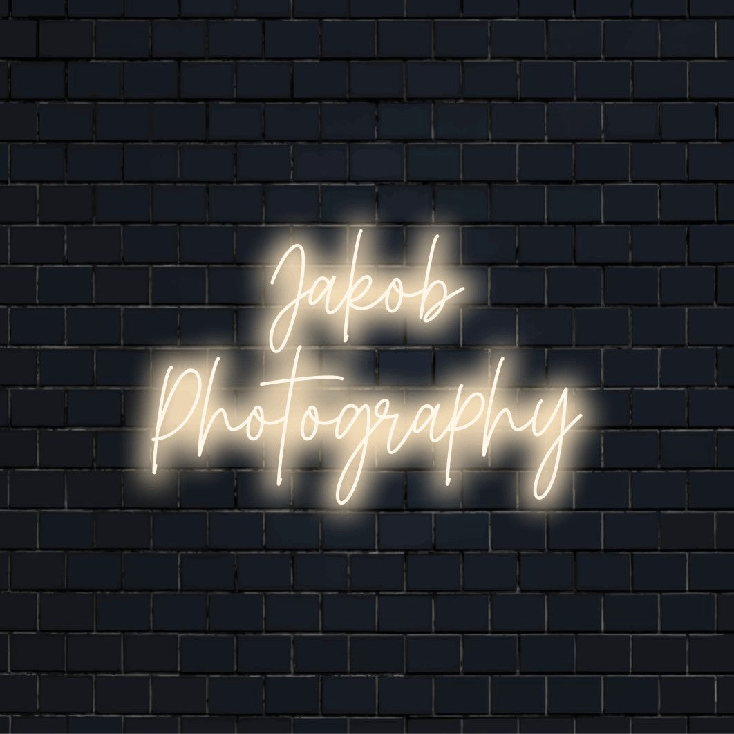 Jakob Photography Custom Name Neon Sign, glowing wall decor on dark brick wall