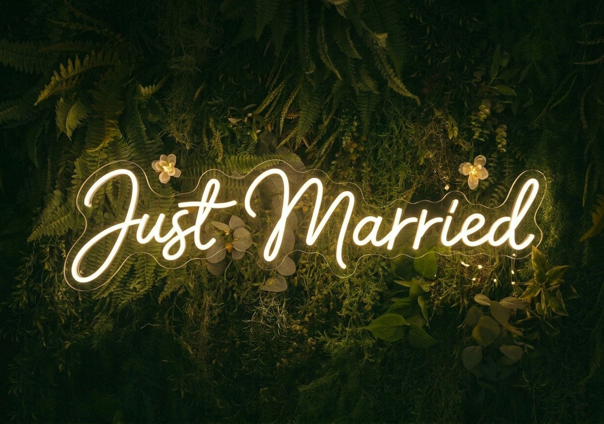 Warmweißes LED-Neonschild mit dem Schriftzug Just Married an einer Pflanzenwand